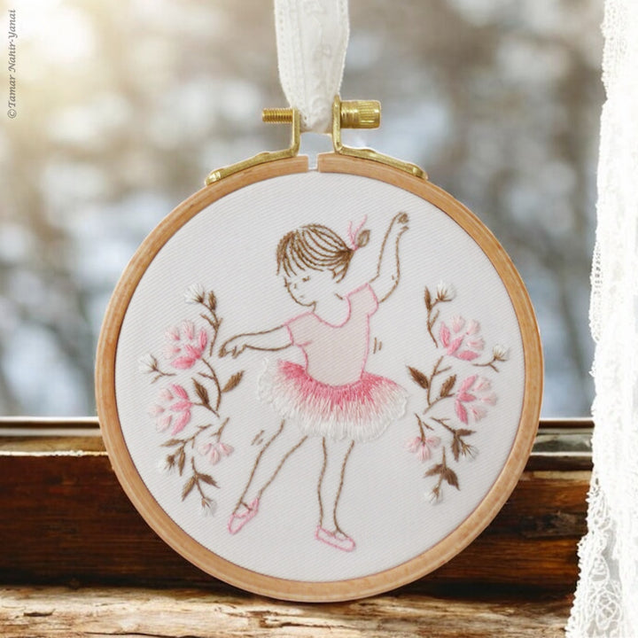 Little Dancer Embroidery Kit features a delicate hand embroidery of a young ballerina in a pink tutu surrounded by soft pink floral accents on white fabric in a wooden hoop.