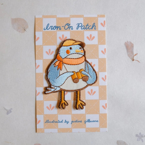 Birder Embroidered Iron-on Patch featuring a cute bird wearing a yellow hat and orange scarf, holding binoculars, designed with colorful thread on a patterned backing card.