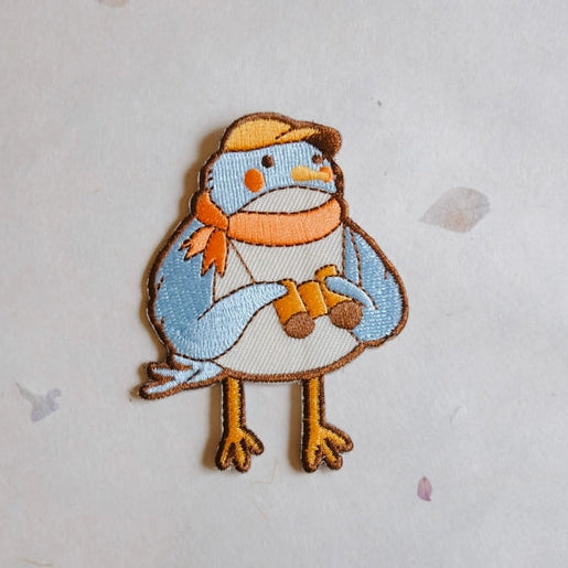 Birder Embroidered Iron-on Patch featuring a cute bird wearing a yellow hat and orange scarf, holding binoculars, made with detailed embroidery thread on fabric.