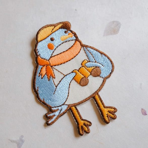 Birder Embroidered Iron-on Patch featuring a cute blue bird wearing an orange scarf and hat, holding binoculars, perfect for adding charm to fabric and modern needlework projects.