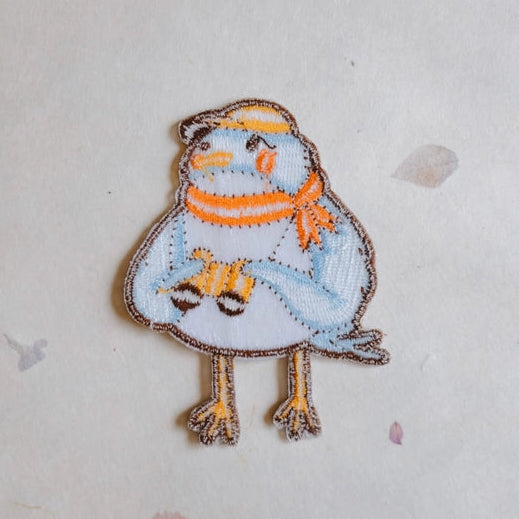 Birder Embroidered Iron-on Patch featuring a blue bird with an orange scarf and yellow beak, designed with detailed stitching suitable for modern needlework and embroidery projects.