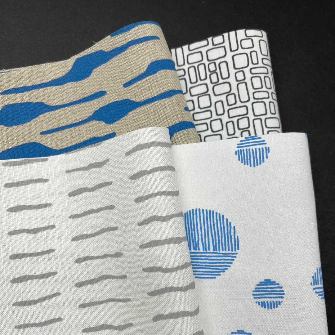 Collection of modern patterned fabrics in shades of blue, grey, and beige displayed in the Colette Moscrop Fabric Sampler Pack, suitable for embroidery and quilting projects.