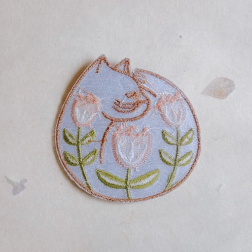Cat Nap Embroidered Iron-on Patch featuring a light blue sleeping cat surrounded by pink tulips with green stems, crafted with fine embroidery floss perfect for modern needlework projects.