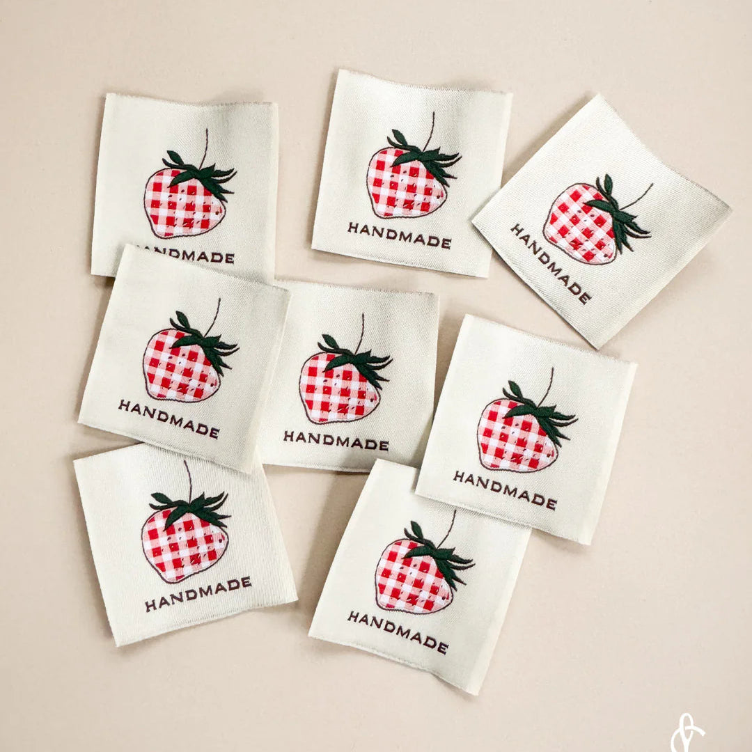 Set of woven labels with strawberry design and 'Handmade' text on a beige background