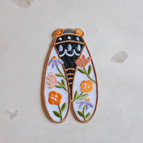 Cicadas Embroidered Iron-on Patch featuring a detailed cicada design with black and orange stitching, decorated with colorful embroidered flowers on a white background.