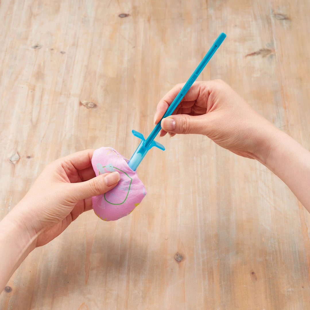 Hands using a blue Tube & Plunger Style Stuffing Tool to fill a small fabric piece, demonstrating precise stuffing for needlework and modern embroidery crafts.