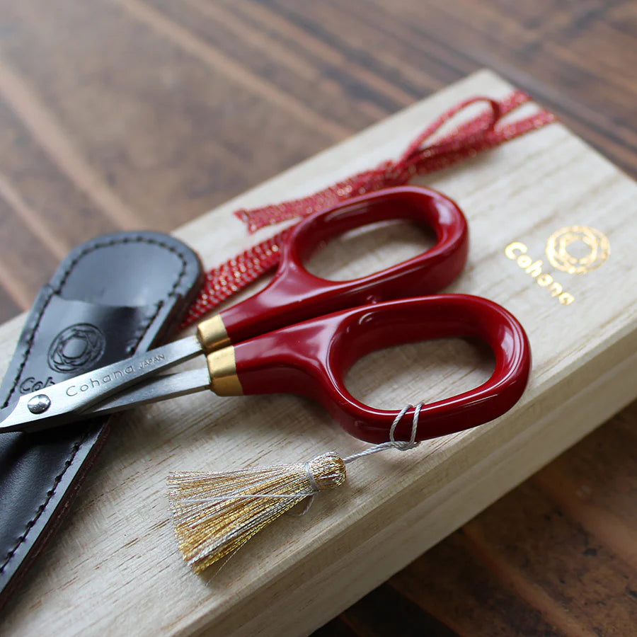 Japanese Artisan Lacquered Handle Embroidery Scissors with deep red handles and gold accents, resting on a wooden box with a leather sheath, ideal for modern needlework and Japanese craft supplies.