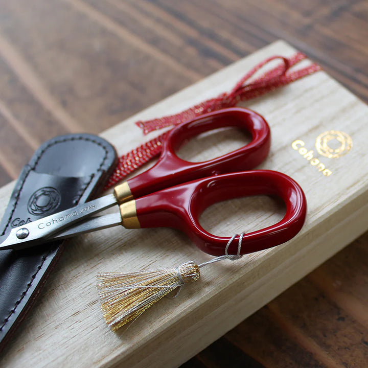Japanese Artisan Lacquered Handle Embroidery Scissors with deep red handles and gold accents, resting on a wooden box with a leather sheath, ideal for modern needlework and Japanese craft supplies.