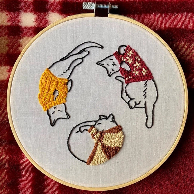Embroidery hoop with embroidered cats in colorful sweaters on a red checkered fabric background