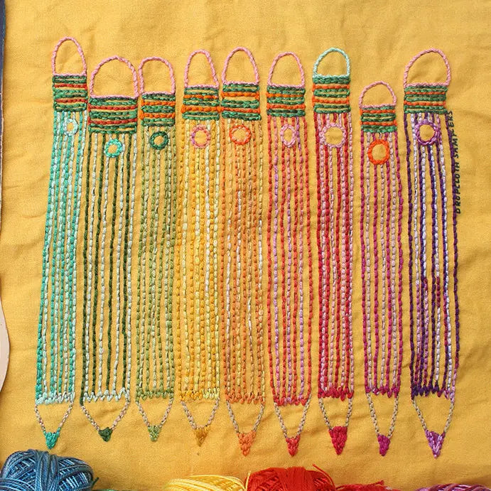 Colorful hand embroidery on yellow fabric shaped like pencils with detailed stitching in green, orange, red, and purple threads, showcasing Pencils Embroidery Sampler using Japanese craft supplies.