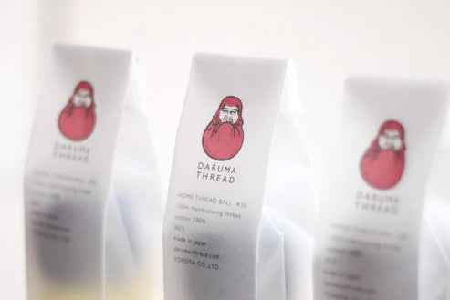 Close-up of packaging featuring Daruma Home Thread #30 Ball Collections with a red daruma doll illustration, highlighting premium Japanese craft embroidery thread supplies.