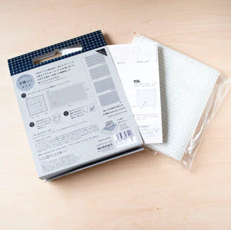 Half-Yard 5mm Straight Line Grid Sashiko Sampler with white fabric featuring a subtle grid pattern, packaged with instructional materials for traditional Japanese sashiko stitching.