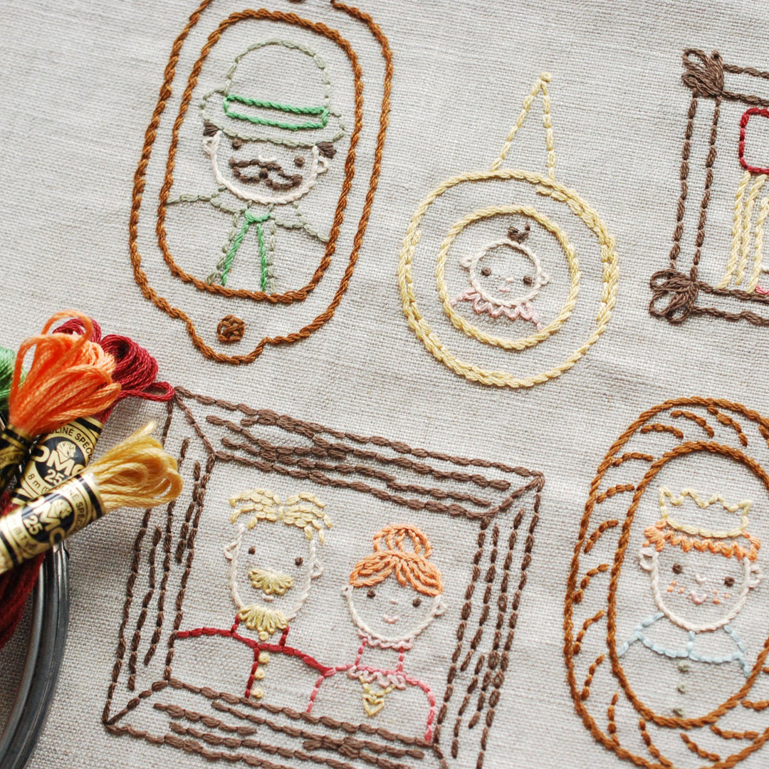 Embroidery project with various portraits and a spool of thread on a textured fabric background.