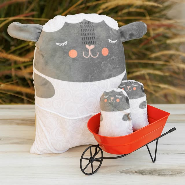 Soft plush sheep pillow and smaller matching plush animals in a red wheelbarrow, crafted from fabric suited for modern needlework, featuring the Farmstead Cuddle Animal Pillow Panel design.