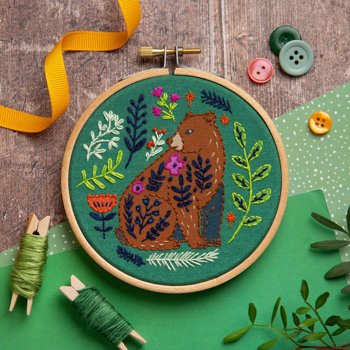 Embroidery hoop with bear design on a wooden surface with buttons and ribbons.