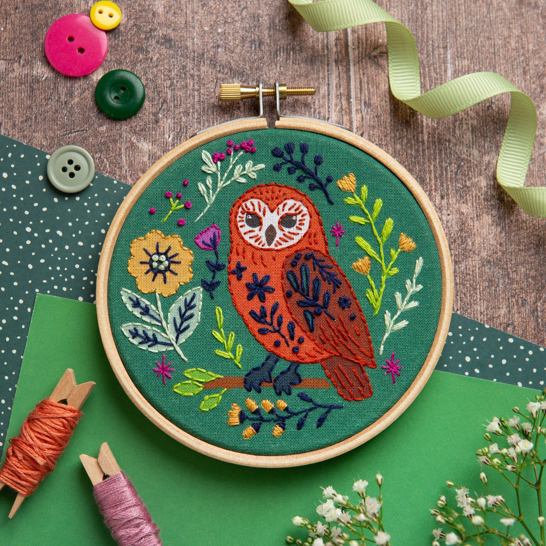 Embroidery hoop with owl design on a wooden surface with buttons and thread spools.