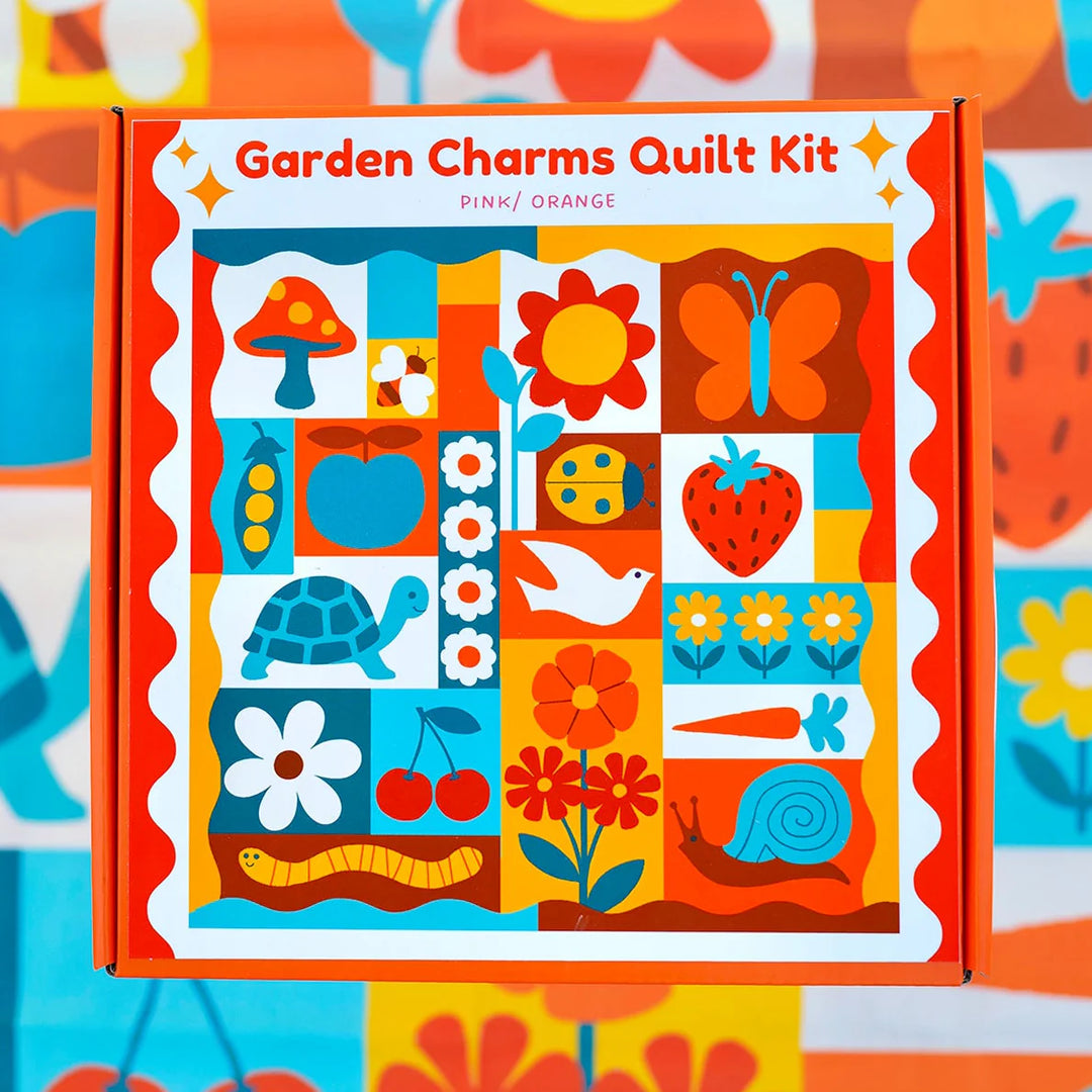 Garden Charms Whole Cloth Quilt Kit featuring colorful, whimsical garden-themed illustrations including flowers, a butterfly, apple, turtle, snail, and other nature-inspired designs in vibrant pink and orange tones.