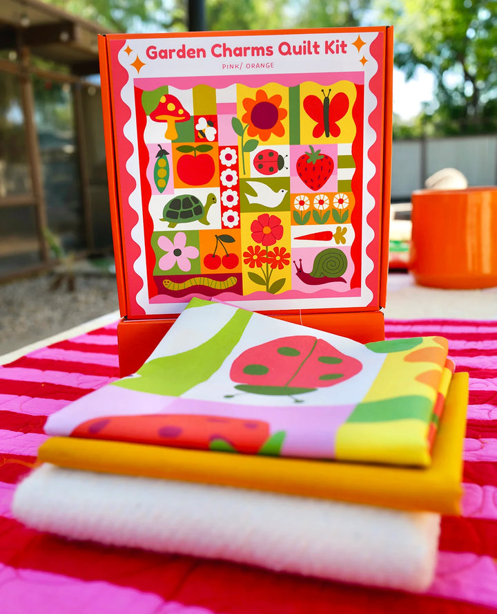 Garden Charms Whole Cloth Quilt Kit featuring colorful fabric pieces with garden-themed prints including ladybugs, flowers, strawberries, and butterflies, ideal for modern needlework and quilting enthusiasts.