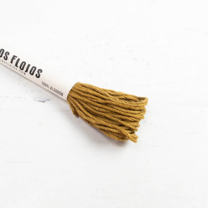 A close-up of a embroidery floss cone with mustard yellow thread wound around a white paper cone printed with the brand name 'Hilos Flojos'.