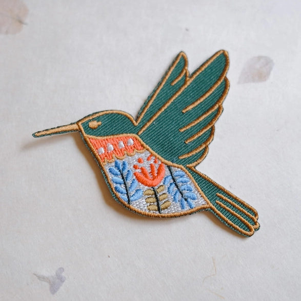 Hummingbird Embroidered Iron-on Patch featuring detailed stitching in green, orange, blue, and tan with a floral pattern, ideal for adding a delicate needlework touch.