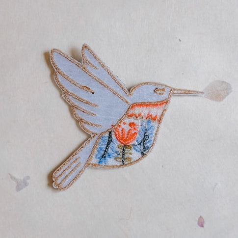 Hummingbird Embroidered Iron-on Patch featuring detailed stitching with light blue, orange, and floral embroidery, perfect for modern needlework and craft projects.