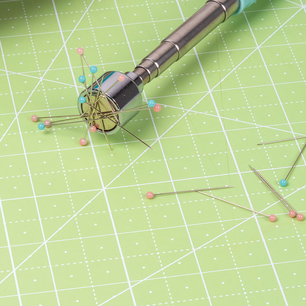 Sewing Magnet Mate holding several colorful sewing pins on a green cutting mat, ideal for keeping needles and pins organized while working on embroidery, quilting, or sewing projects.