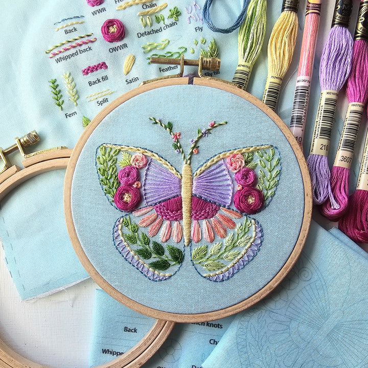 Beginner Butterfly Sampler Hand Embroidery Kit featuring a colorful butterfly embroidered on blue fabric with embroidery floss and pattern guide visible, perfect for modern needlework enthusiasts.