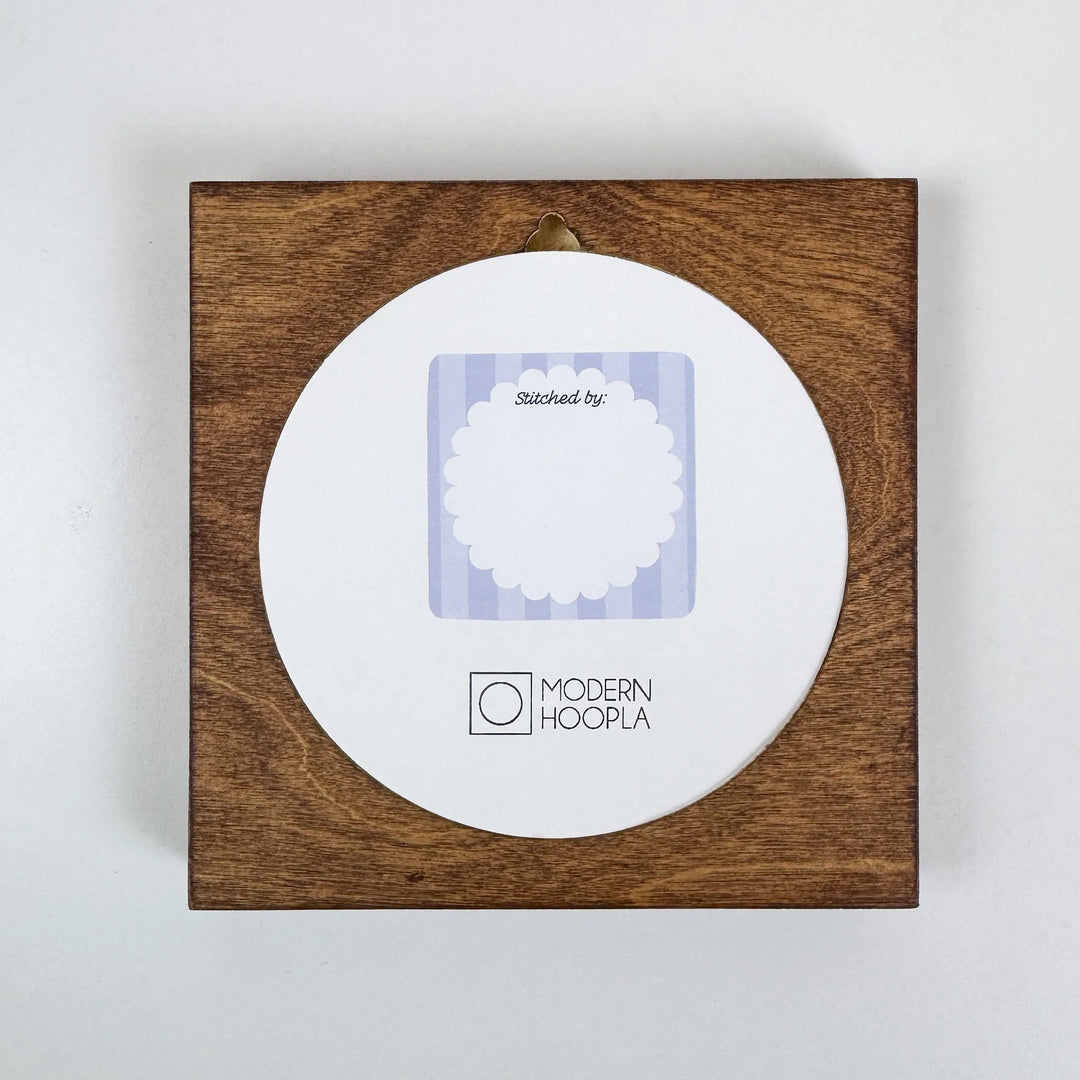 Made By" Project Label Sticker Pack featuring a round sticker with scalloped edge and text "Stitched by:" on a wooden background, ideal for modern needlework projects.