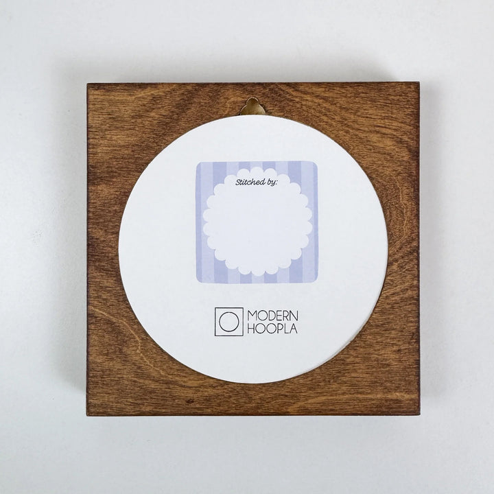 Made By" Project Label Sticker Pack featuring a round sticker with scalloped edge and text "Stitched by:" on a wooden background, ideal for modern needlework projects.