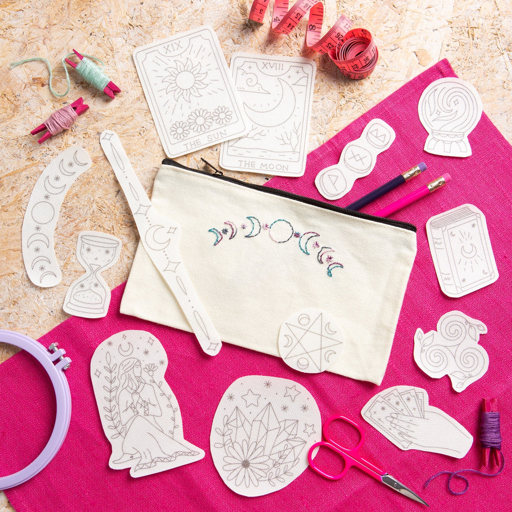 Crafting materials including templates, fabric, and sewing tools on a pink surface.