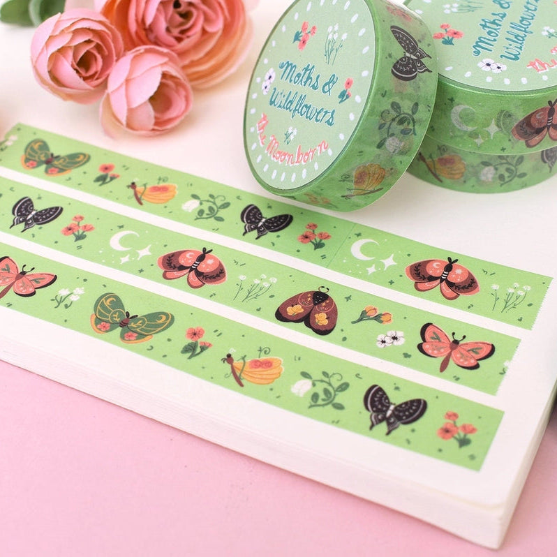 Green washi tape rolls and strips with a 'Maths & Wildflower' butterfly and flower pattern, displayed on a white tray with pink roses on a pink and blue background.