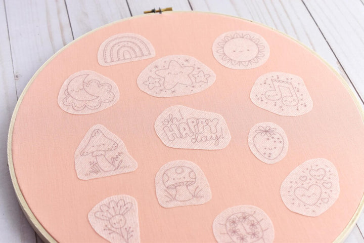 Embroidery hoop with various embroidered shapes on a pink background