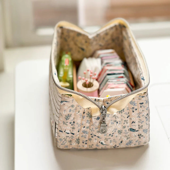 Fabric storage bin with a zipper, containing stationery items on a light surface.