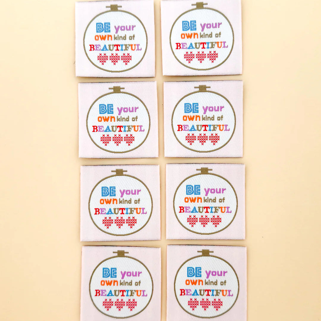 Set of eight motivational woven labels with 'Be your own kind of beautiful' text on a beige background