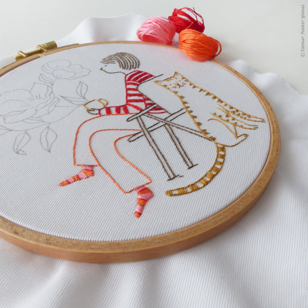 Me & My Tiger Embroidery Kit showing a hand-stitched design of a person sitting on a chair with a tiger on their back, using vibrant embroidery floss on white fabric.