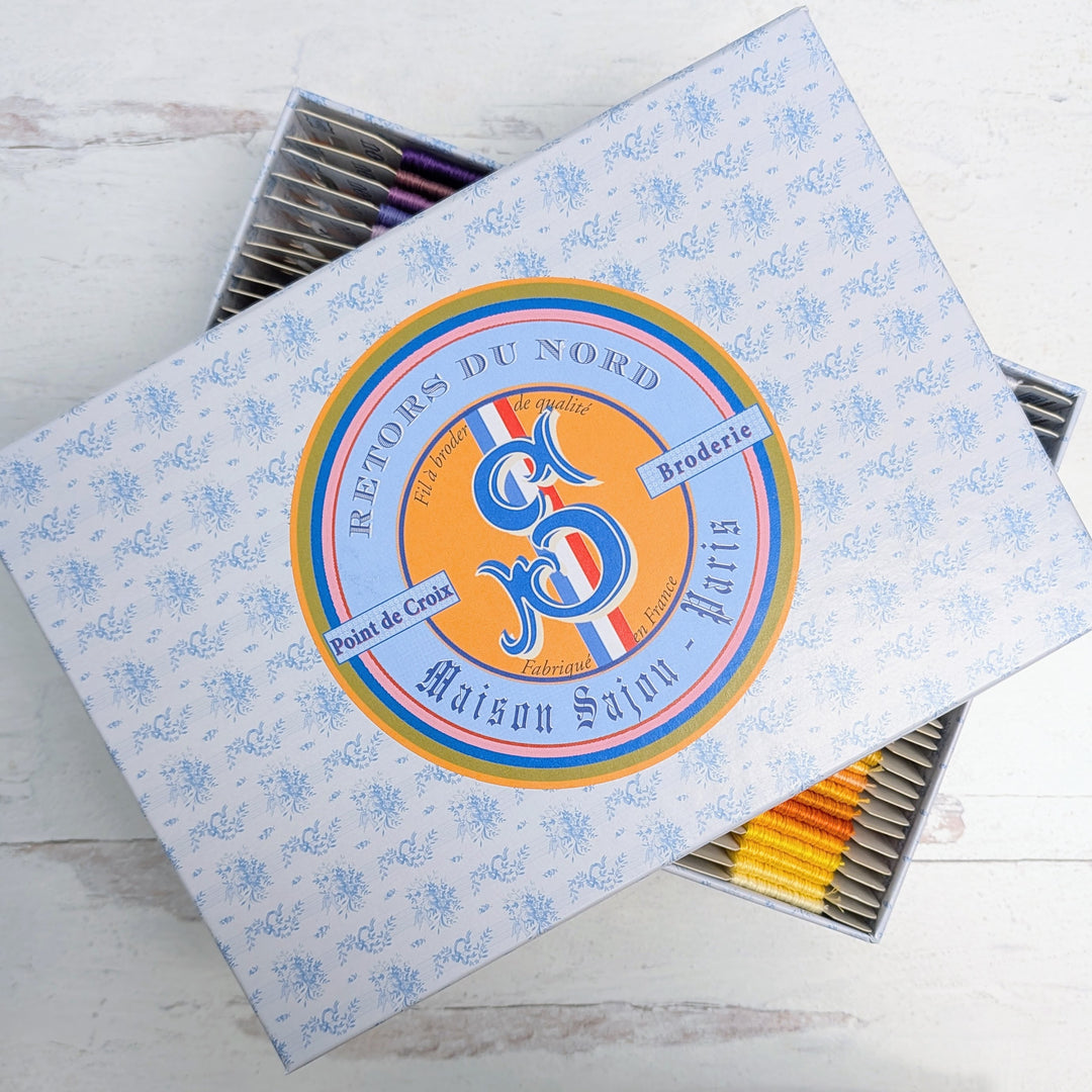 Retors du Nord French Embroidery Floss - Complete Set in a decorative box featuring a floral pattern, showcasing vibrant embroidery threads in purple, yellow, and orange shades.