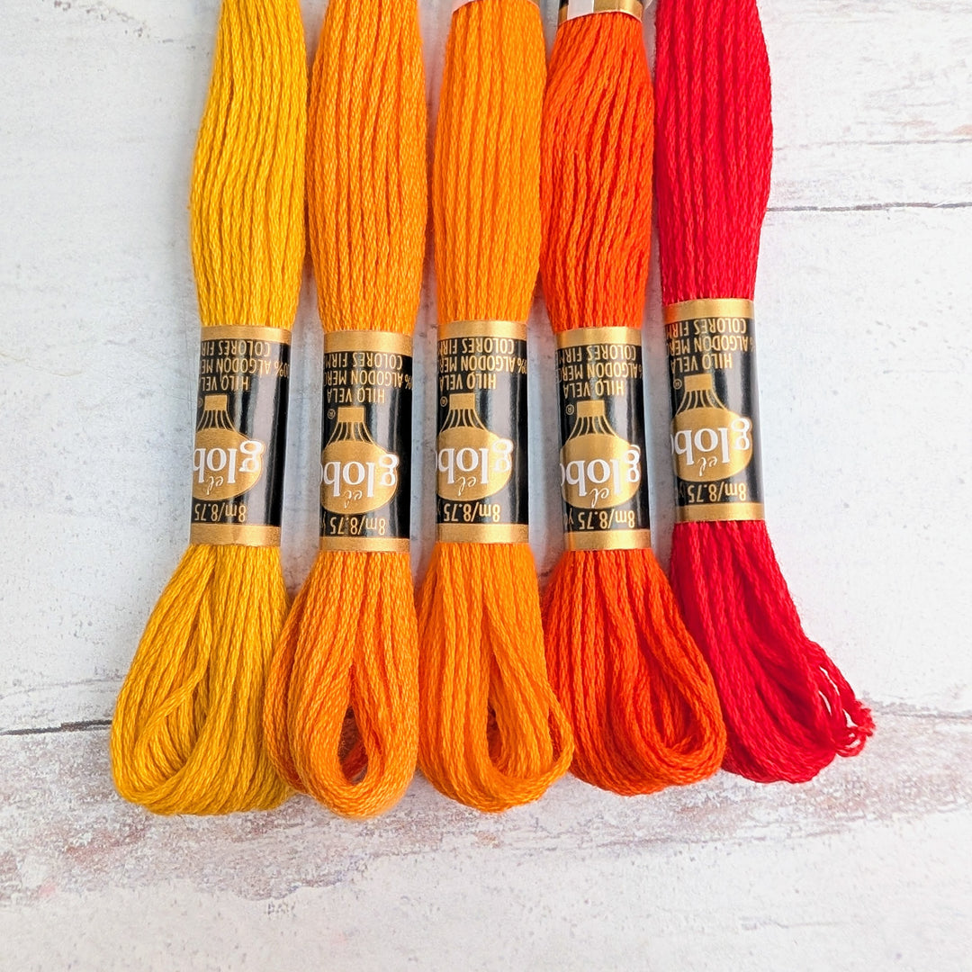 Five skeins of Hilo Vela El Globo Embroidery Thread (8m Skeins) - Orange in varying shades from yellow to red, neatly arranged on a light wooden surface.