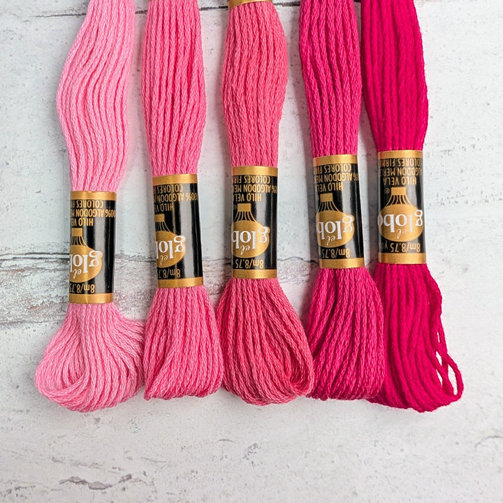 Five skeins of Hilo Vela El Globo Embroidery Thread (8m Skeins) - Pink in varying shades of pink arranged on a light textured surface, showcasing smooth, high-quality embroidery floss for needlework projects.