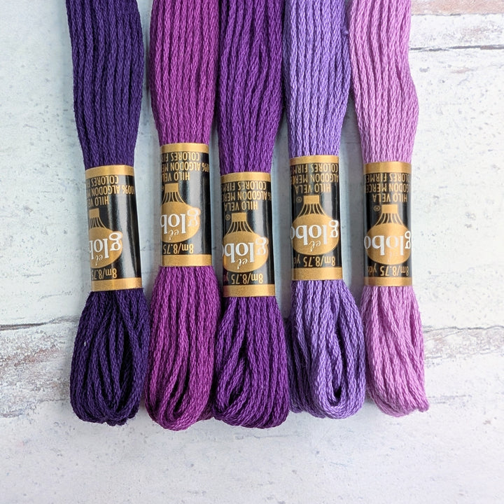 Five skeins of Hilo Vela El Globo Embroidery Thread (8m Skeins) - Purple in varying shades laid out on a light surface, ideal for modern needlework and Japanese craft supplies.