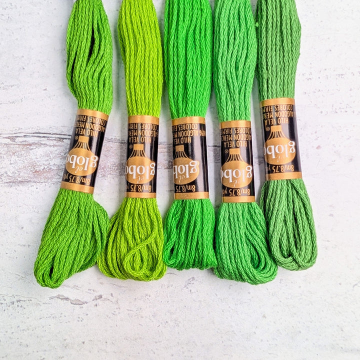 Five skeins of Hilo Vela El Globo Embroidery Thread (8m Skeins) - Bright Green in various shades of vibrant green arranged side by side on a light textured surface, ideal for modern needlework and Japanese craft supplies.