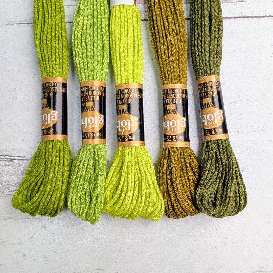 Five skeins of Hilo Vela El Globo Embroidery Thread (8m Skeins) - Muted Green in varying shades from light to dark green, laid out on a white surface for modern needlework and Japanese craft supplies.