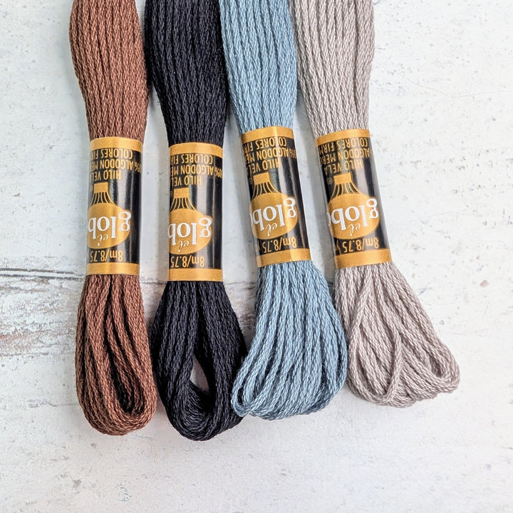 Four skeins of Hilo Vela El Globo Embroidery Thread (8m Skeins) - Neutrals in shades of brown, black, blue, and beige laid side by side on a white surface, ideal for embroidery and modern needlework projects.