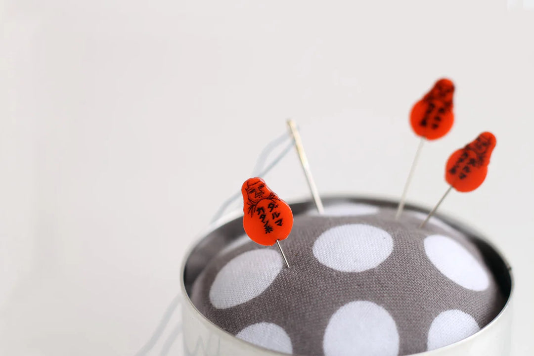 Artisan Made Japanese Pin Cushion with gray fabric featuring white polka dots, decorated with red-headed sewing pins, ideal for embroidery and modern needlework crafts.