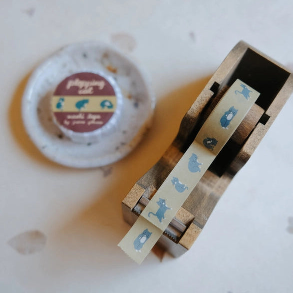 Plopping Cat Washi Tape featuring a cream background with blue cat illustrations, displayed in a wooden tape dispenser on a white surface, ideal for Japanese stationery and craft projects.
