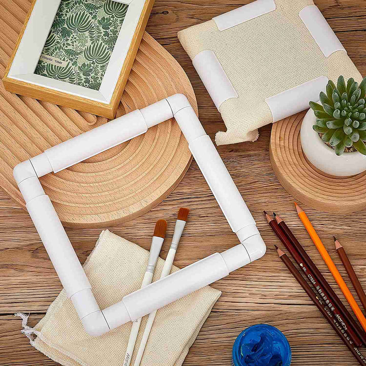 two qsnap frames artfully aranged on a desktop. One of the frames has a piece of off white aida cloth inside of it. there are pencils and paintbrushes on the desk beneath the frames