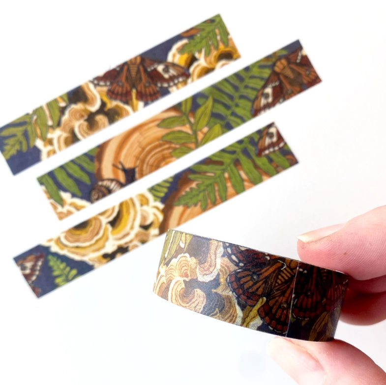 Hand holding a roll of Mushroom Grove Washi Tape featuring intricate designs of mushrooms, ferns, and butterflies in earthy tones, perfect for Japanese craft supplies and needlework projects.