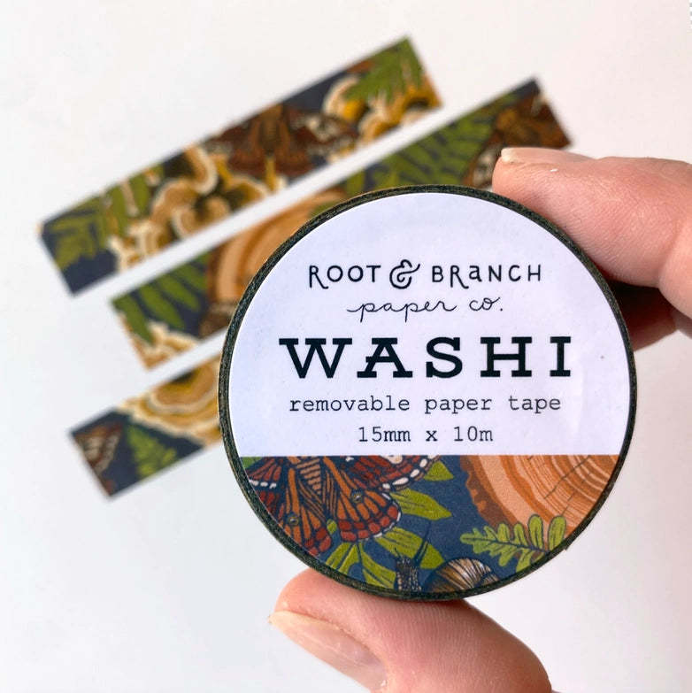 Hand holding a roll of Mushroom Grove Washi Tape with botanical and mushroom patterns, alongside strips of the decorative tape in autumn tones, suitable for Japanese craft supplies and modern needlework projects.
