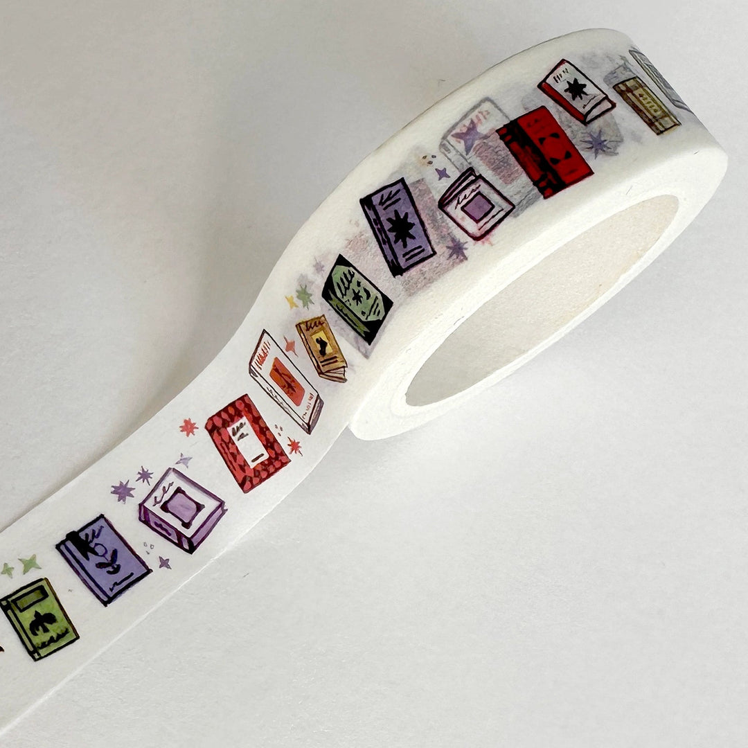 A roll of white washi tape featuring a colorful pattern of vintage cassette tapes in red, purple, green, yellow, and black, photographed on a plain white background.