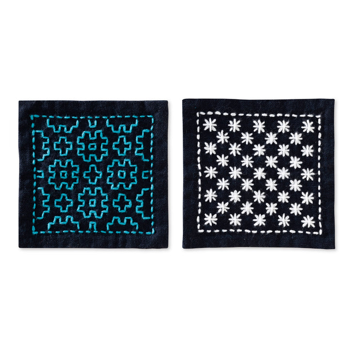 Two navy fabric coasters featuring traditional Japanese Hitomezashi Sashiko embroidery patterns in blue and white thread from the Beginner Hitomezashi Sashiko Coaster Kit - Navy (SK-479).