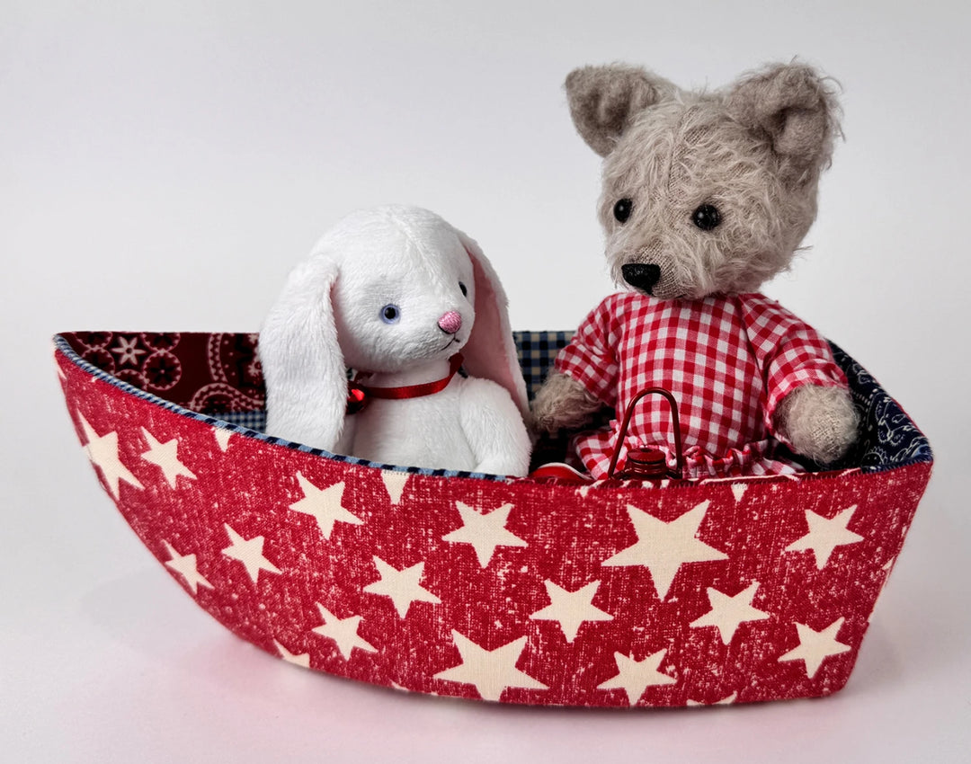 Soft fabric boat with star pattern holding a handmade plush bunny and wolf, crafted using the English Paper Piecing Bowls Pattern - The Dory Boat, showcasing modern needlework.